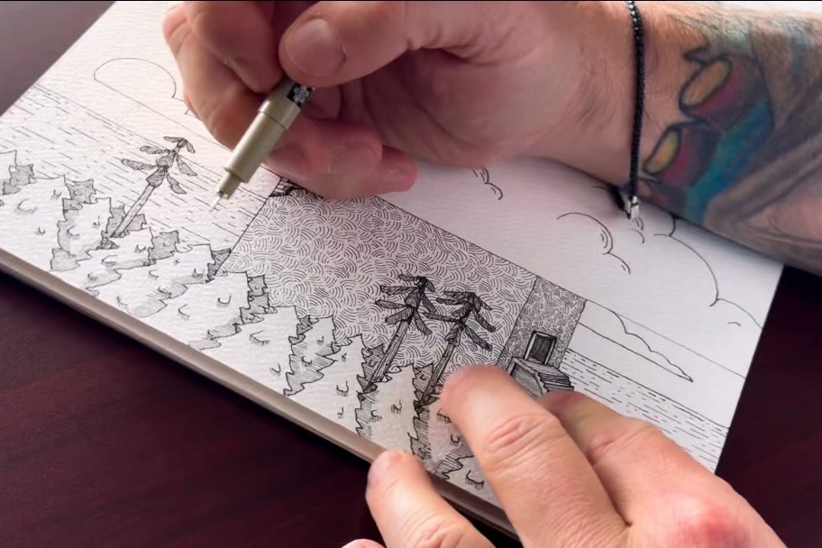 Close view of Adam Allegrucci drawing texture and shading into a pen-and-ink scene with trees and an aged building